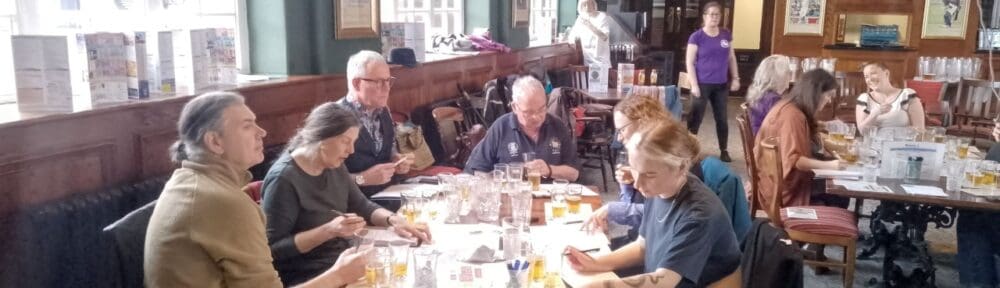 Volunteer judges sitting at tables in a pub function room, tasting and scoring beers during judging