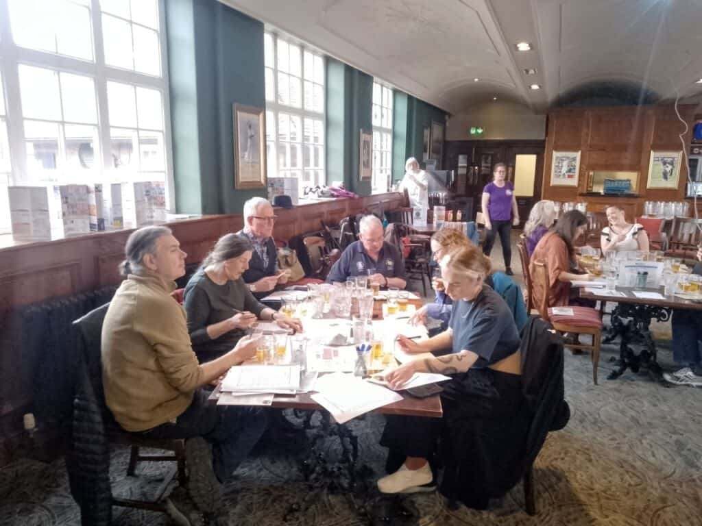 Volunteer judges sitting at tables in a pub function room, tasting and scoring beers during judging